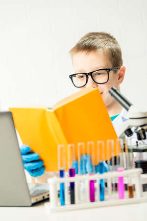 A schoolboy with a microscope and book examines chemicals in test tubes, conducts experiments - a portrait on a white background. Concept for the study of  in the laboratoryの写真素材