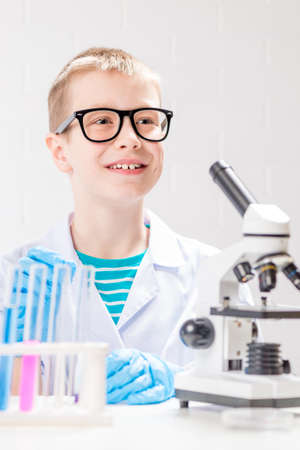 A schoolboy with a microscope examines chemicals in test tubes, conducts experiments - a portrait on a white background. Concept for the study of coronavirus in the laboratoryの写真素材