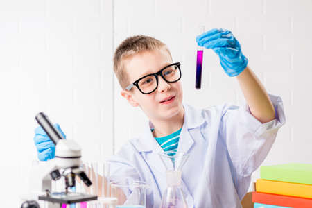 A schoolboy with a microscope and book examines chemicals in test tubes, conducts experiments - a portrait on a white background.の写真素材