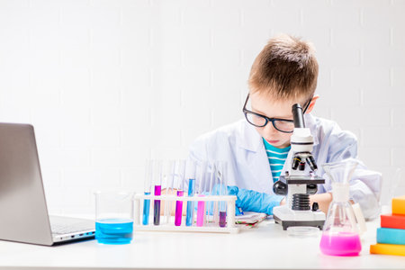 A schoolboy with a microscope examines chemicals in test tubes, conducts experiments - a portrait on...