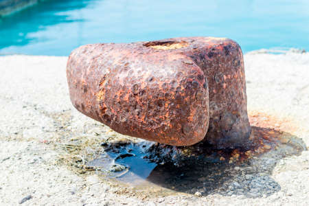 Single, old and rusty mooring bollard on the pier with a view on seaの写真素材
