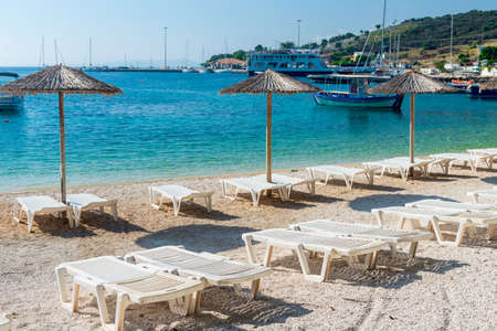 Summer vacation destination. Straw sunshades and sunbeds on the empty beach with sea in the background.の写真素材