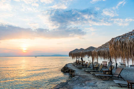 Beautiful sunset seascape with beach chairs and umbrella on the coast, Greeceの写真素材