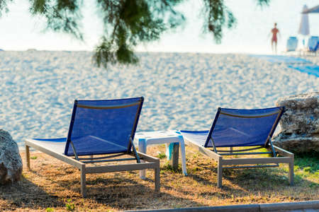 Two deckchairs on the beach with bright sun and wavesの写真素材