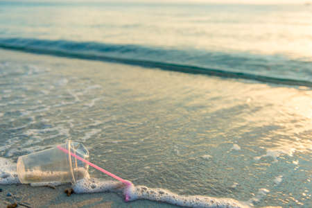 Disposable plastic glass discarded on sandy sea coast ecosystem,nature pollution