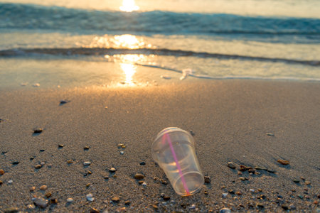 Disposable plastic glass discarded on sandy sea coast ecosystem,nature pollutionの写真素材