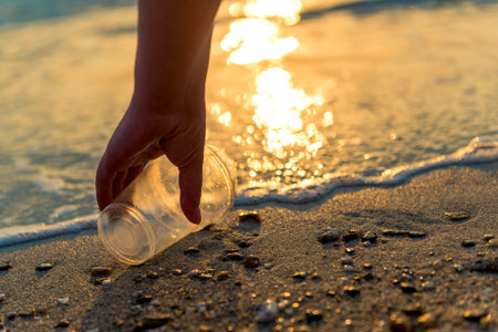 A hand cleaning and picking up a plastic glass trash on the beachの写真素材