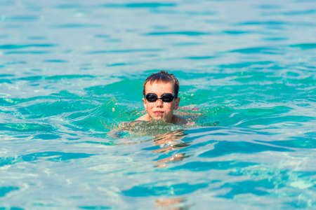 A boy is swimming and having fun in the sea near the shore in swimming gogglesの写真素材
