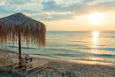 Beautiful sunset seascape with beach chairs and umbrella on the coast, Greeceの写真素材