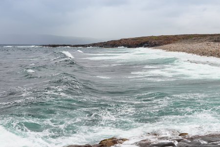 Dangerous sea wave crashes on a rocky coastline with splashes and foam before a storm in the Barents Seaの写真素材