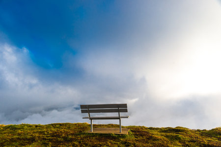 A picturesque landscape with a bench on the edge of a cliff against the background of beautiful thick clouds high in the mountains.の写真素材