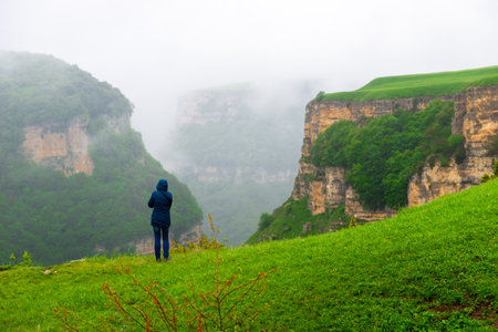 A man admires the beautiful view of the misty canyon in bad weather. The mountains of the North Caucasus. Russia.の写真素材
