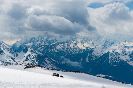 A dramatic view of the rocky white peaks of the mountains of the North Caucasus range from the snow-covered slope of Mount Elbrus in a storm. Caucasusの写真素材