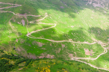 Winding mountain serpentine on the slope of a green mountain under the shadow of cloudsの写真素材