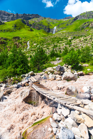 An old, flimsy wooden bridge across a turbulent, full-flowing mountain river with a fast current. Caucasus, Elbrus region.の写真素材