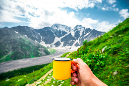 First person view with hand holding yellow cup against picturesque mountain view. North Caucasusの写真素材