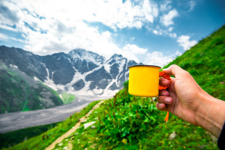 First person view with hand holding yellow cup against picturesque mountain view. North Caucasusの写真素材