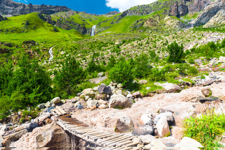 An old, flimsy wooden bridge across a turbulent, full-flowing mountain river with a fast current. Caucasus, Elbrus region.の写真素材