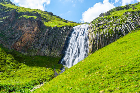 Beautiful Terskol waterfall falls from a basalt wall and is surrounded by green slopes. Caucasus, Elbrus region.の写真素材