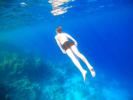 Boy snorkeling dive deep into the blue sea near the coral reef. Red Seaの写真素材