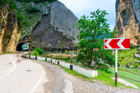 Turn direction sign on a mountain asphalt road against the background of a tunnel in a rocky mountain. North Turn direction sign on a mountain asphalt road against the background of a tunnel in a rocky mountain. North Caucasusの写真素材