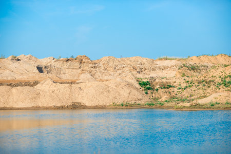 View of the slopes of the shore of a sand quarry filled with water on a sunny dayの写真素材
