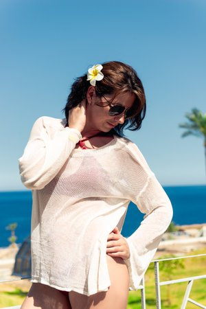 Beautiful girl in a white tunic poses against the backdrop of a warm tropical sea in sunny weatherの写真素材