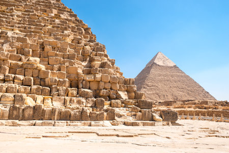 A ruined corner of the majestic Egyptian pyramid of Cheops with the Pyramid of Khafre in the background under the scorching sun of the Sahara Desert. Cairoの写真素材