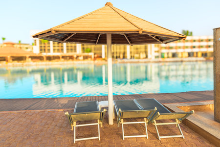 Sun loungers and umbrella by the pool with clear azure water in the tropicsの写真素材
