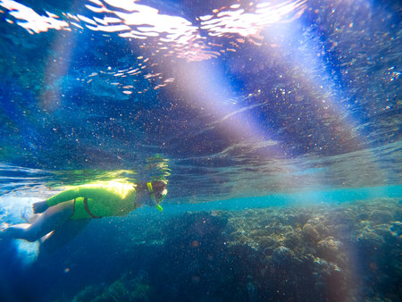 A woman in a green swimsuit and mask swims underwater exploring the corals of the Red Sea. Snorkelingの写真素材