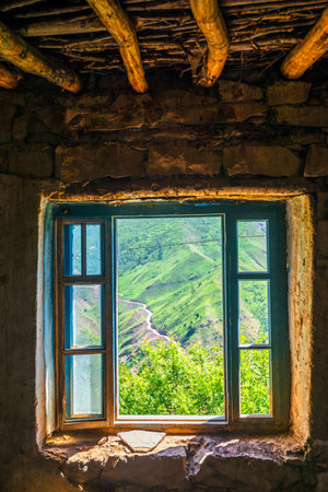 Picturesque view of a mountain slope through the window of an old house. North Caucasus