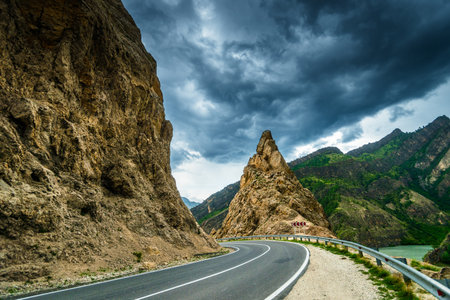 Dramatic mountain landscape with a curved mountain road on the edge of a cliff in a river valley....