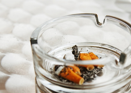 Cigarette butts in a glass ashtray, smoking in public placesの写真素材