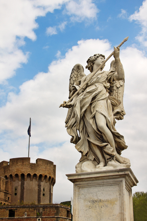 Marble statue of angel with spear by Bernini on Saint Angelo Bridge against the background of Castel Sant'Angelo in Rome, Italyの写真素材