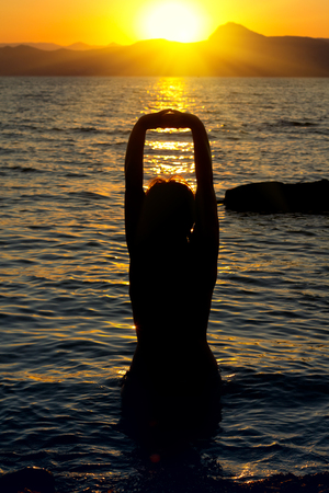 Young woman is practicing yoga on the sea beach at sunset の写真素材