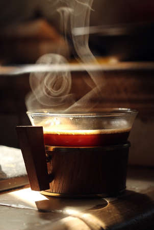 Small glass cup of hot black coffee with smoke on table. Dark background.の写真素材
