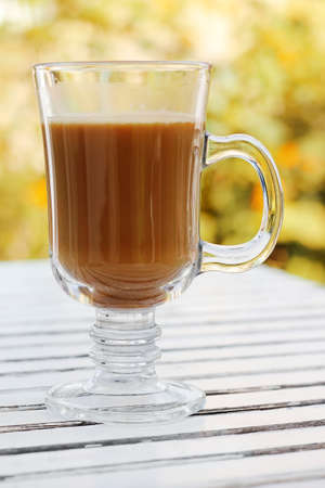 Glass cup of latte coffee on white wooden table outdoors at autumn.の写真素材