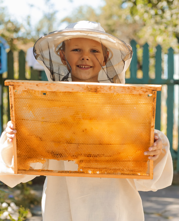Young beekeeper boy holding frame of honeycomb.の写真素材