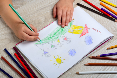 The child draws his family on a piece of paper with colored pencils. What can a childrens picture tell. The concept of child psychology.の写真素材