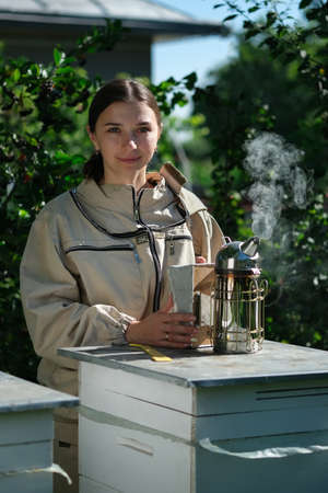 Portrait of a beautiful young female beekeeper working in an apiary near beehives with bees. Collect honey. Beekeeper on apiary. Beekeeping concept.の写真素材