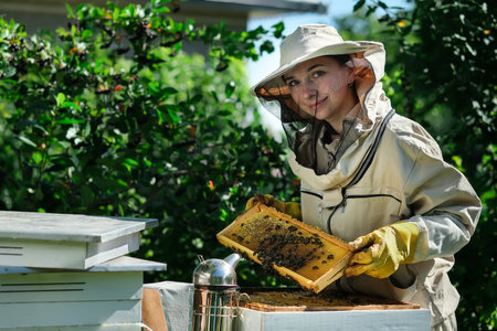 Portrait of a beautiful young female beekeeper working in an apiary near beehives with bees. Collect honey. Beekeeper on apiary. Beekeeping concept.の写真素材