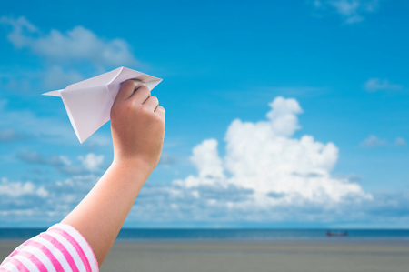 plane paper in children hand over seaand blue sky in cloudy dayの写真素材