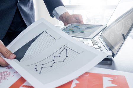 Business, office concept. businessman working with digital tablet and laptop with financial business document on dark brown desk.の写真素材