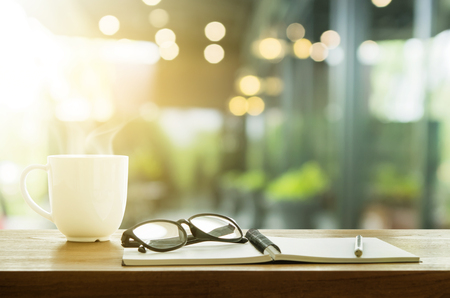 Cup of coffee and note book on wooden table. Coffee break in morning, selective focus.の写真素材