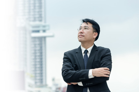 Portrait of asian businessman with arms crossed standing with city building background.の写真素材