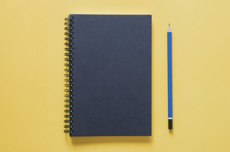 Office workplace minimal concept. Black notebook and pencil on yellow background. Top view with copy space, flat lay. Pastel color filter.の写真素材