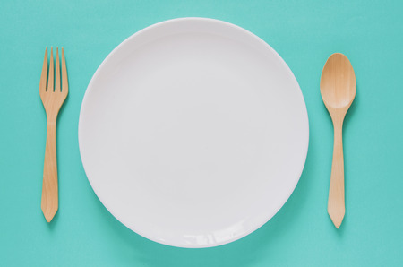 Dinner minimal background concept. Top view of empty white plate with wooden fork and spoon on blue background. Flat lay.の写真素材