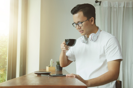 Young asian man drinking coffee and using digital tablet in coffee shop. Business online concept.の写真素材