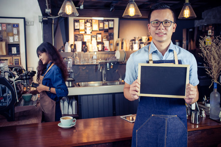 Portrait of smiling asian barista holding blank chalkboard menu in coffee shop. Cafe restaurant service, Small business owner, food and drink industry concept.の写真素材