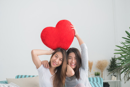 Lovely lesbian couple together concept. Couple of young women holding pillow in form heart with happiness moment.の写真素材